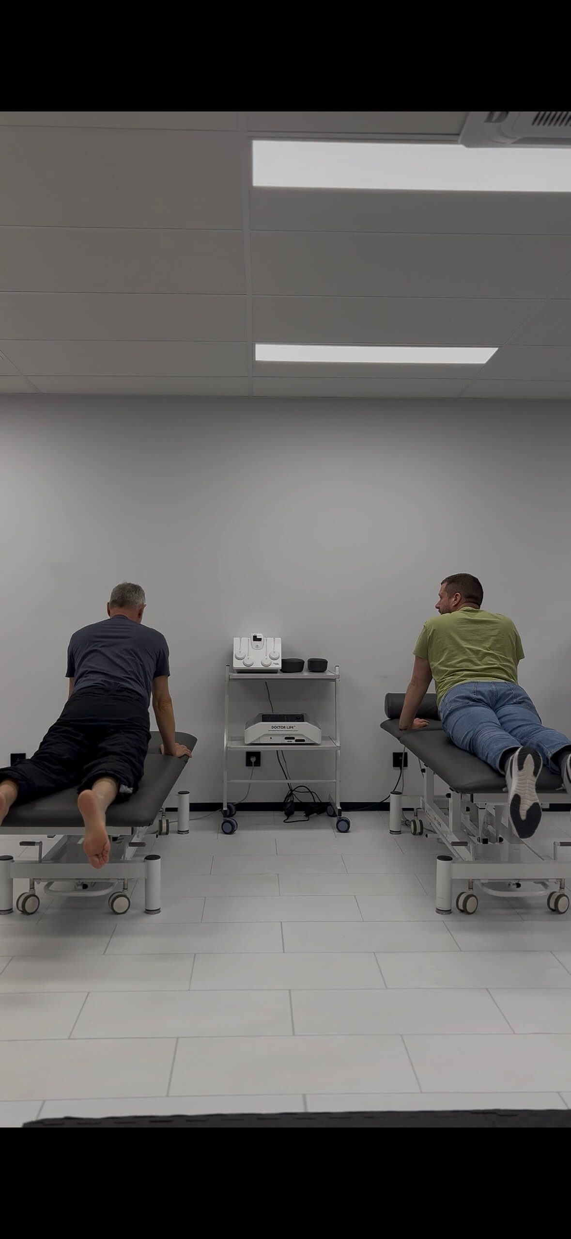Deux patients en extension lombaire en décubitus ventral (press-up McKenzie) en cabinet de kinésithérapie à Tournai — exercice utilisé comme reset neuromoteur pour libérer l'inhibition fessière
